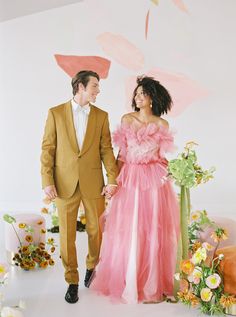 a man and woman standing next to each other in front of a floral wallpaper