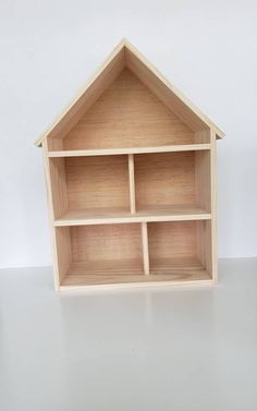 a wooden doll house with shelves on the top and bottom shelf, in front of a white wall