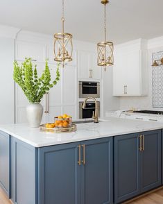 a kitchen with blue cabinets and white countertops, gold pendant lights over the island