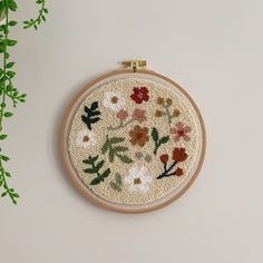 the embroidery is hanging on the wall next to a potted plant with green leaves