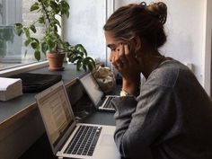 a woman sitting at a desk with two laptops on her lap and a cell phone to her ear