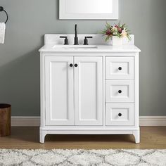 a white bathroom vanity with drawers and a mirror on the wall above it, in front of a gray wall