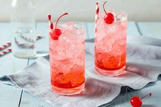 two glasses filled with ice and cherries on top of a napkin next to a bottle of water