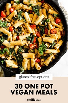 a skillet filled with pasta, spinach and tomatoes on top of a table