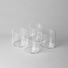 four clear glass cups sitting next to each other on a white surface with no one around them