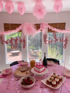 a table topped with cakes and desserts under pink balloons