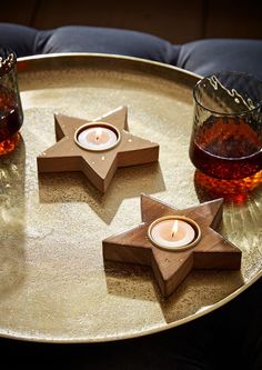 three wooden star shaped tea lights on a metal tray with two glasses and one candle