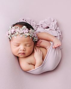 a newborn baby wearing a flower headband laying on her side in a purple wrap