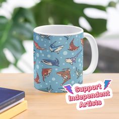 a blue mug with sharks on it sitting next to some books and a plant in the background