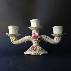 a white candelabra with three candles on it's sides and pink flowers