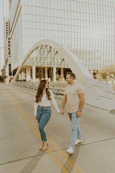 a man and woman holding hands while walking down the street in front of a large building