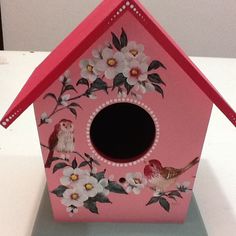 a pink birdhouse with flowers painted on it's side and two birds in the center