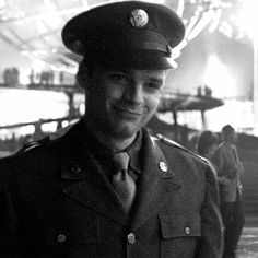 a black and white photo of a man in uniform smiling at the camera with other people behind him