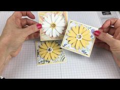 two hands are holding small cards with yellow and white flowers on them, while another person holds