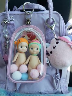 two little dolls are sitting in front of a pink purse with key chains attached to it