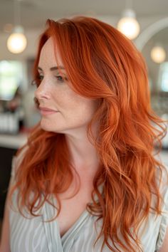 Woman with long, wavy red hair wearing a light-colored top, looking to the side in a softly lit setting. Copper Red Hair, Natural Curly Hair Cuts, Red Balayage