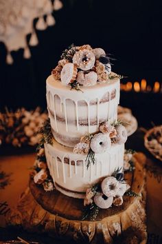 a three tiered cake with frosting and flowers sitting on top of a wooden slice