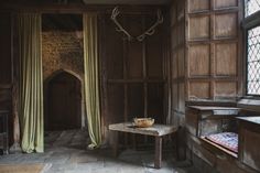 an old room with wood paneling and curtains on the window sill, a bowl of fruit sits on a table in front of it