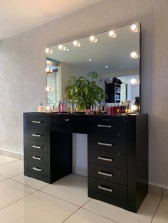 a black vanity with lights on it and a potted plant in front of the mirror