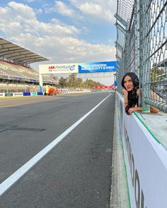 a woman leaning on the side of a fence next to a race track with a sky background