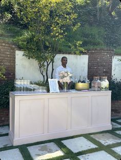 a man sitting at a table with flowers and vases on it in front of a brick wall