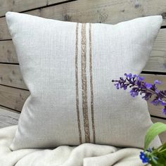 a white pillow sitting on top of a wooden bench next to a vase with purple flowers