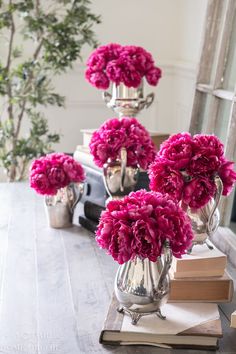 pink flowers in silver vases sitting on top of a wooden table next to books