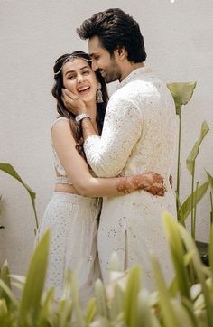 a man and woman standing next to each other in front of some tall green plants