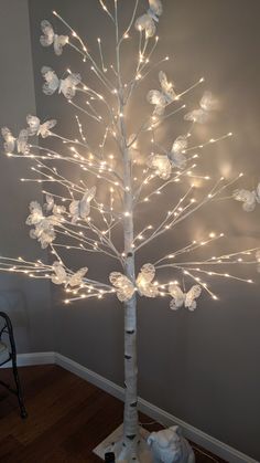 a lighted tree with white branches and flowers on the top is in front of a gray wall