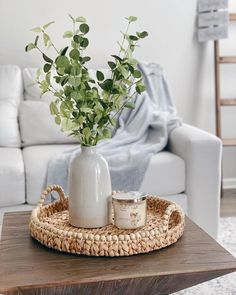 a white vase filled with green leaves sitting on top of a wooden table next to a couch