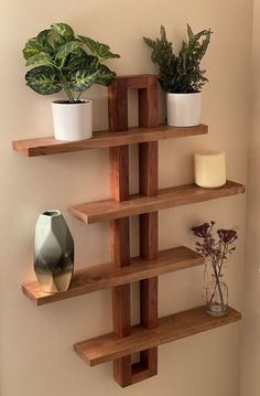 three wooden shelves with plants and candles on them in the corner of a room next to a wall