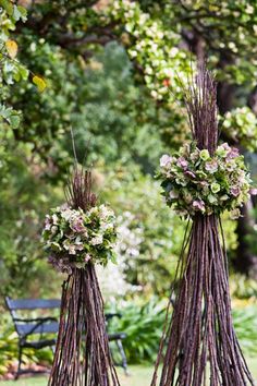 two sticks with flowers hanging from them in the middle of a park area next to a bench