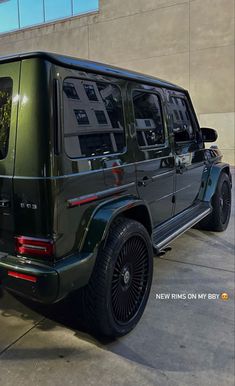 a green mercedes g - class parked in front of a building