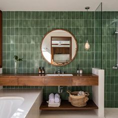 a bathroom with green tiles and a wooden counter top, along with a round mirror above the sink