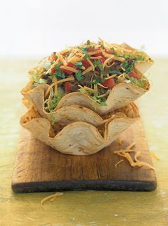 a tortilla dish with meat, cheese and lettuce in it on a wooden cutting board