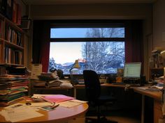 an office with a desk, computer and bookshelf in front of a window