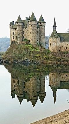 an old castle sitting on top of a hill next to a body of calm water