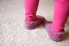 a person wearing pink pants and crocheted slippers standing on carpeted floor