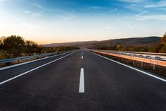 an empty highway with two lanes leading into the distance and trees on both sides at sunset