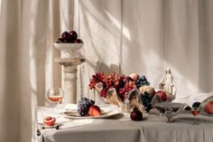 an arrangement of fruit on a table in front of a white drapeed curtain