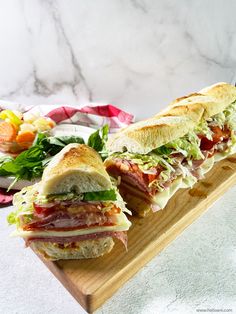 two sub sandwiches sitting on top of a wooden cutting board