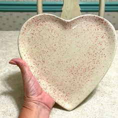 a hand holding a heart shaped dish on top of a kitchen counter next to a chair