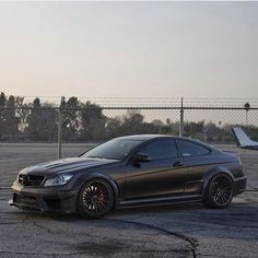 a black car parked in front of a fence on top of an airport tarmac