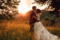 a bride and groom are standing in tall grass at sunset with the sun behind them