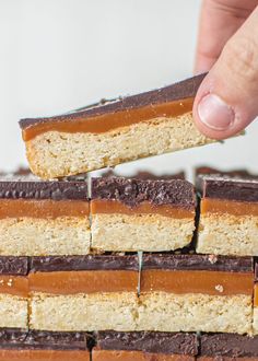 a hand picking up a piece of cake from a stack