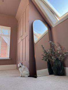 a white cat sitting in front of a large mirror next to a vase with flowers