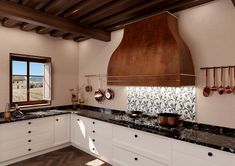 a large kitchen with white cabinets and black counter tops, an island style stove hood and copper pots on the wall