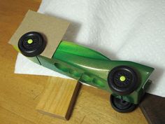 a green toy car sitting on top of a wooden table next to a white towel