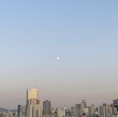 a city skyline with tall buildings and a full moon in the sky over it's horizon