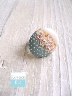 a polka dot ring with pink flowers on it sitting on a wooden table next to a sticker that says kovacs eva